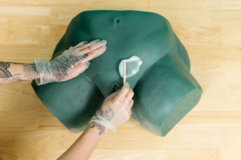 Esthetician's hands applying wax to Sayge to train a brazilian wax pattern