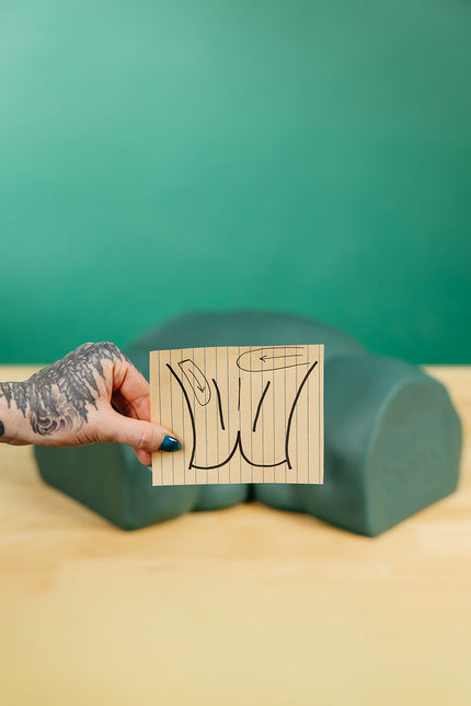 Hand holding 2D brazilian wax pattern instructions in front of Sayge the 3D wax training model