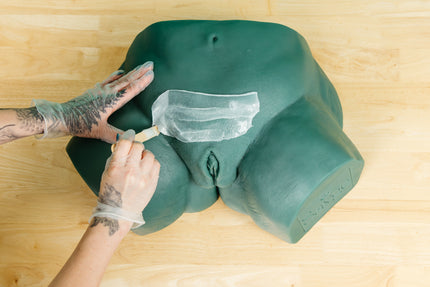 Esthetician applying wax to Sayge's pubic mound against a wooden surface